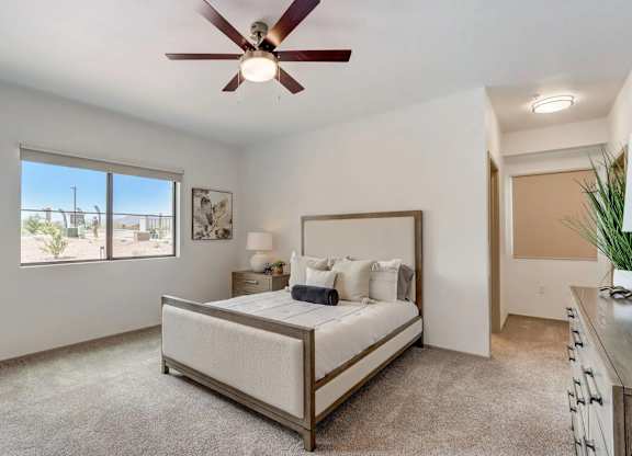 A bedroom with a bed, a ceiling fan, and a window overlooking a patio.