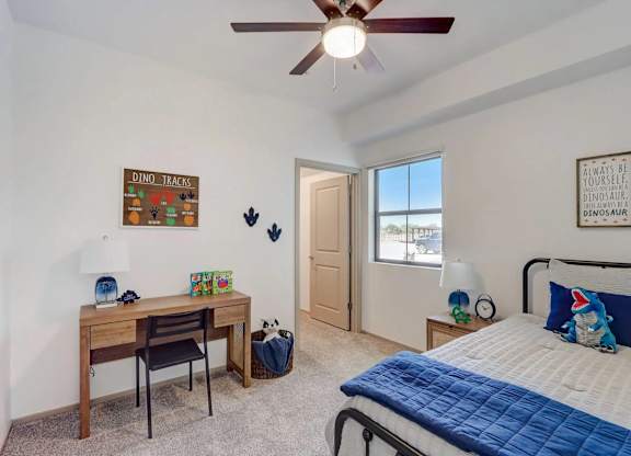 A bedroom with a bed, desk, and a ceiling fan.