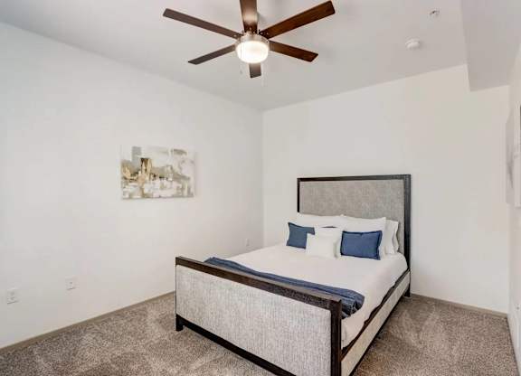 A bedroom with a bed, pillows, and a ceiling fan.