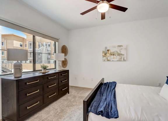 A bedroom with a white bed, a brown dresser, and a ceiling fan.