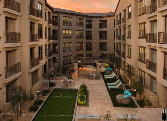 A sunset view of a courtyard with a green lawn and apartment buildings.