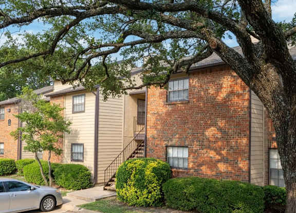 A tree in front of a brick building with a car parked in front of it.