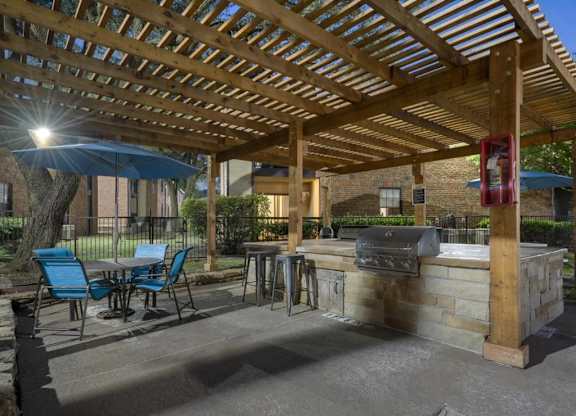 A wooden pergola with a blue umbrella and chairs.