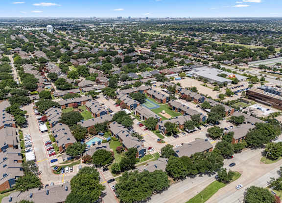 A bird's eye view of a residential area with houses, cars, and trees.