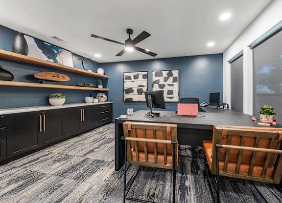 A room with a desk, chairs, and a ceiling fan.