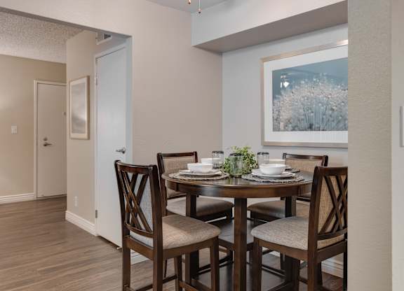 A dining room with a table set for two and a painting on the wall.