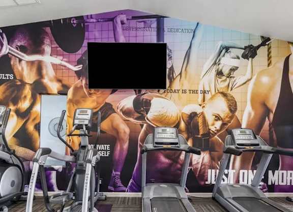 A gym with treadmills and exercise equipment in front of a wall with fitness motivational posters.