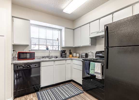 A kitchen with a black refrigerator and white cabinets.
