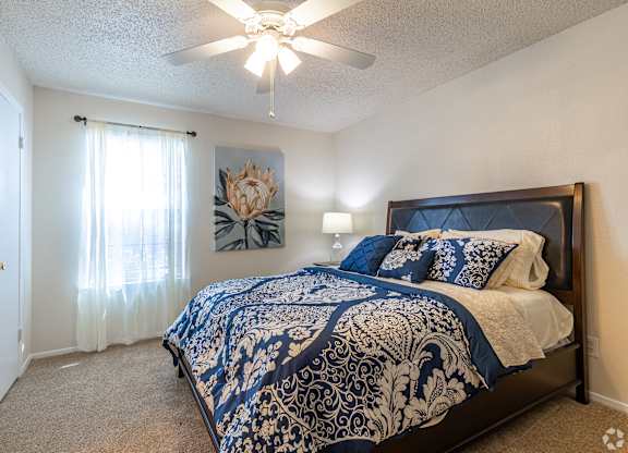A bedroom with a bed, a ceiling fan, and a painting on the wall.