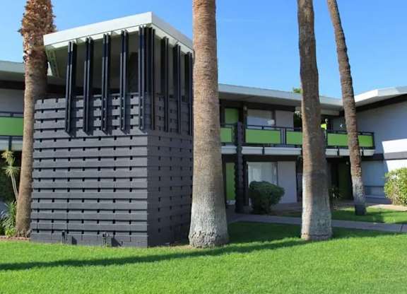 A modern building with a flat roof and a grey facade is surrounded by palm trees.