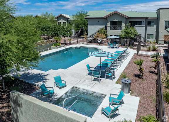 A pool with blue chairs and a hot tub in front of a building.