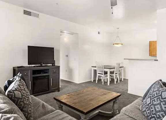 A living room with a grey couch, a wooden coffee table, a television, and a dining table with chairs.