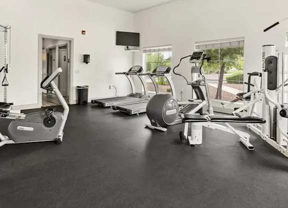A spacious gym with treadmills, elliptical machines, and a fan.