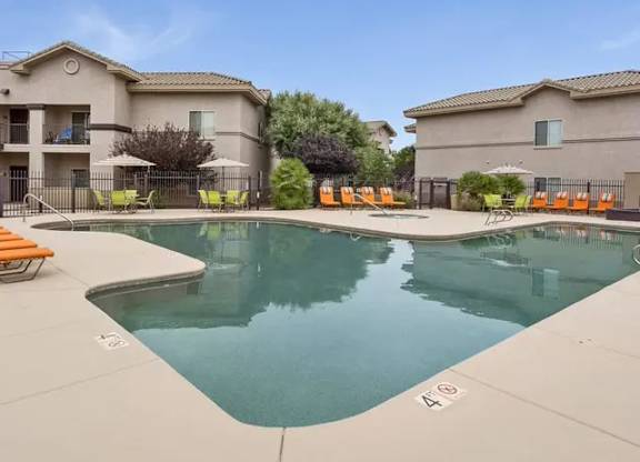 A large swimming pool surrounded by orange lounge chairs and apartment buildings.