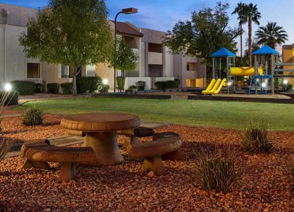 A playground with a slide and a picnic table is lit up at dusk.