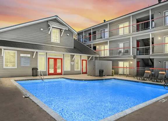 A swimming pool in front of a building with a sunset in the background.