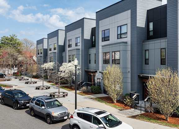 A row of modern townhouses with cars parked in front.