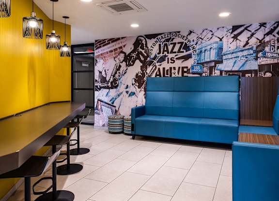 A blue couch is in the middle of a room with a yellow wall and a mural on the wall.