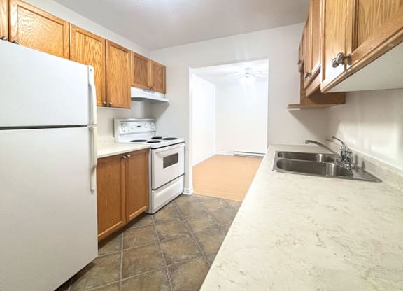 A kitchen with a white refrigerator, wooden cabinets, and a marble countertop.