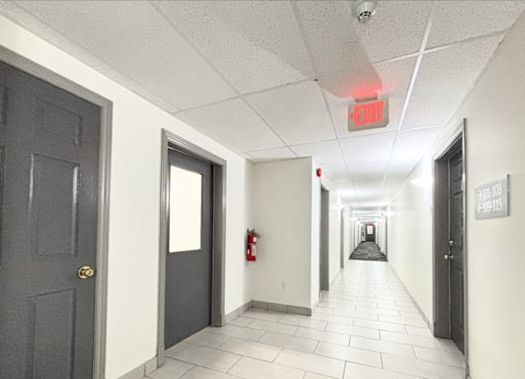 A long hallway with doors on either side and a red exit sign above.