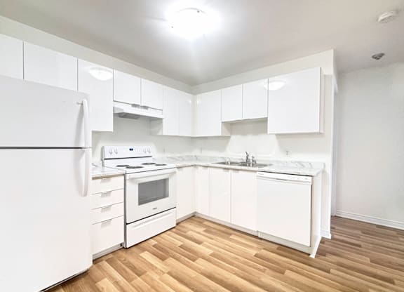 A white kitchen with wooden floors and white appliances.
