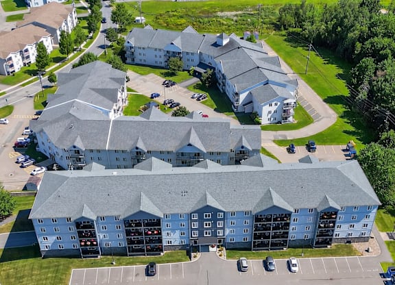 A large building with a grey roof and a parking lot in front.