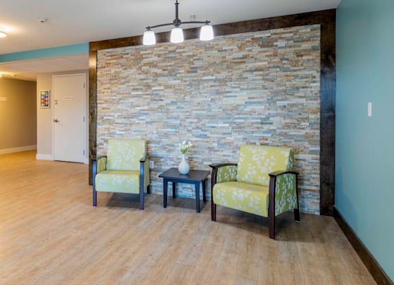 Two chairs and a table are in a room with a stone wall.