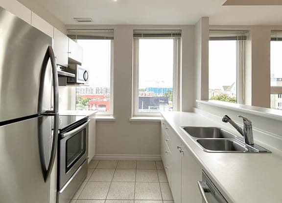 A kitchen with a stainless steel refrigerator and a window overlooking a cityscape.