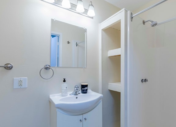 A white bathroom with a sink, mirror, and shower.