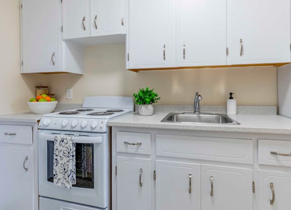A white kitchen with a stove, sink, and cabinets.