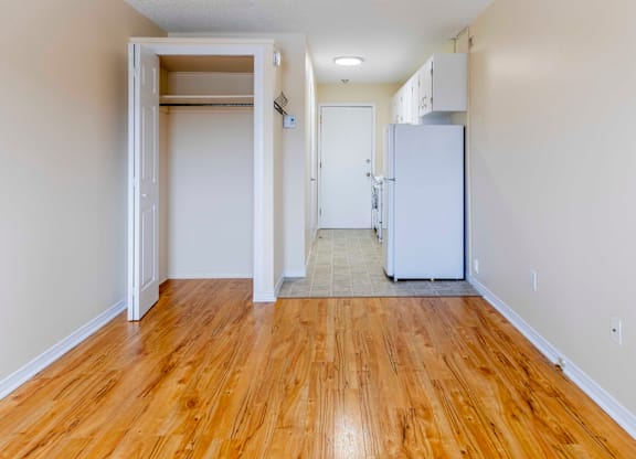 A room with a white fridge and wooden floors.