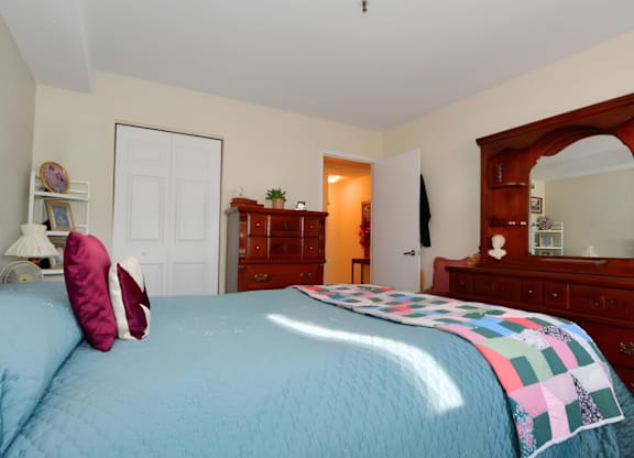 A bedroom with a blue bedspread and a wooden dresser.