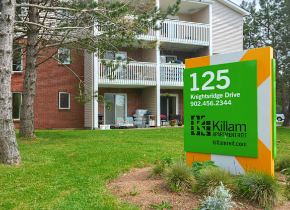 A sign for Killam Apartment Rent in front of a building.