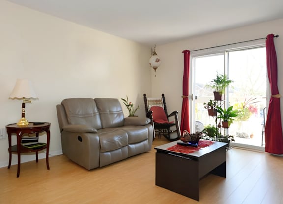 A living room with a grey leather sofa, a wooden side table with a lamp, a red chair, and a black coffee table.