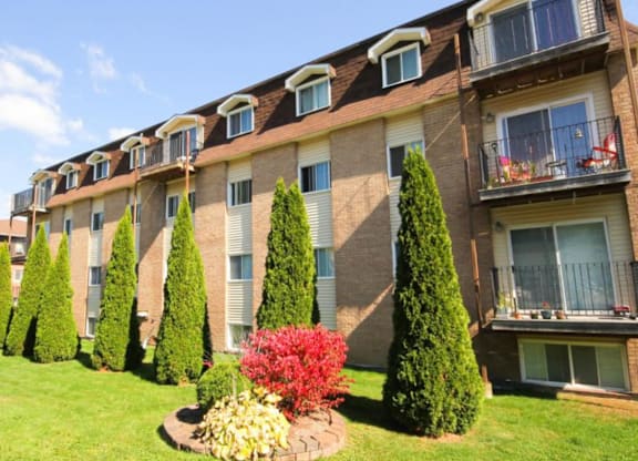 A row of apartment buildings with balconies and trees in front.