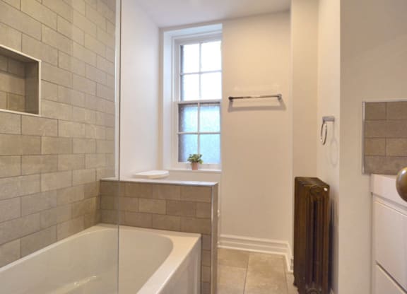 A bathroom with a tub, window, and radiator.