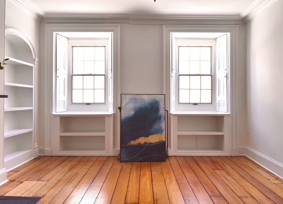 A room with a painting in the middle and two windows.