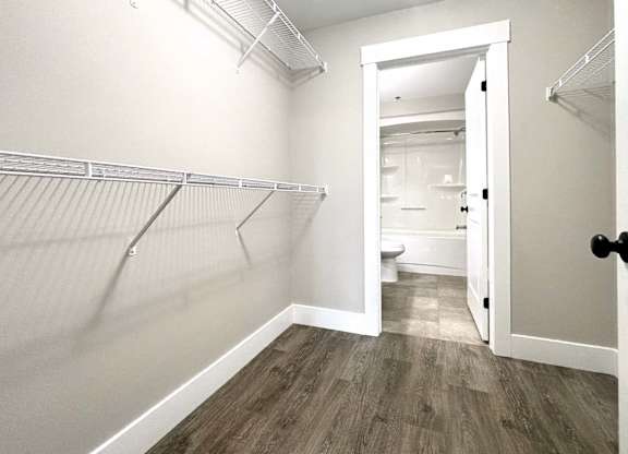 A white walk in closet with a doorway leading to a bathroom.