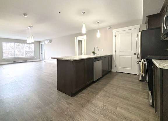 A kitchen with a dark brown island and light wood flooring.