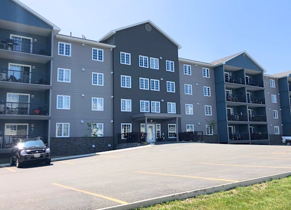 A black car is parked in a parking lot in front of a large apartment building.