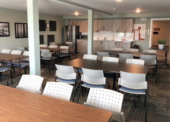 A cafeteria with tables and chairs and a kitchen in the background.