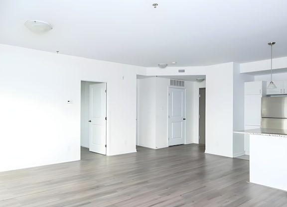 A white room with a wooden floor and a kitchen area in the background.