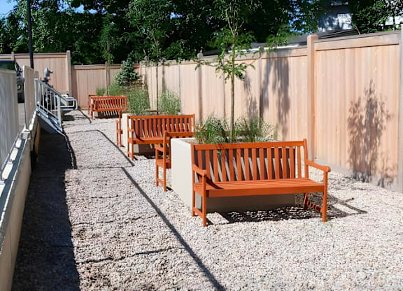 A row of orange benches are lined up on a gravel path.