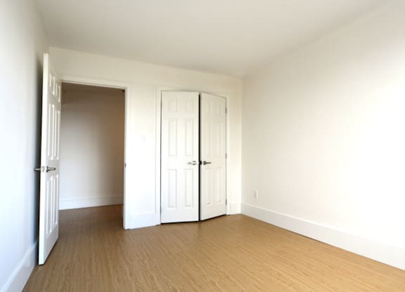 A room with white walls and wooden flooring with two white doors.
