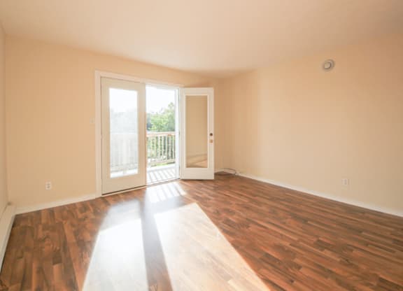 A room with wooden floors and a door leading to a balcony.