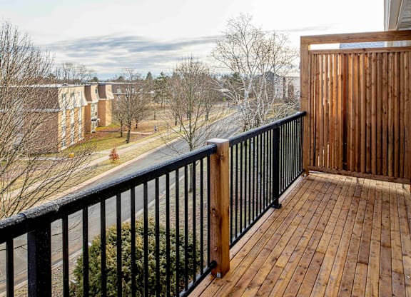 A balcony with a black railing and wooden floor overlooks a residential area.