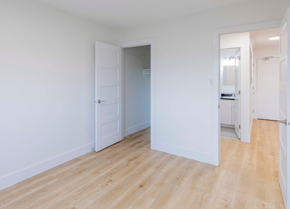 A room with white walls and wooden flooring with a door open to another room.