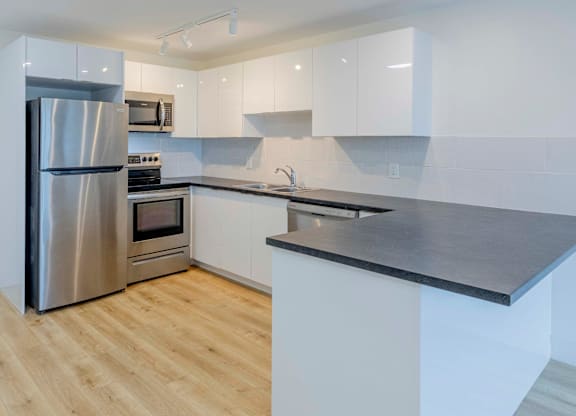 A modern kitchen with a stainless steel refrigerator and wooden flooring.