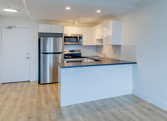 A modern kitchen with a stainless steel refrigerator and wooden flooring.