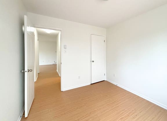 A room with white walls and wooden flooring with a door on the left and a window on the right.